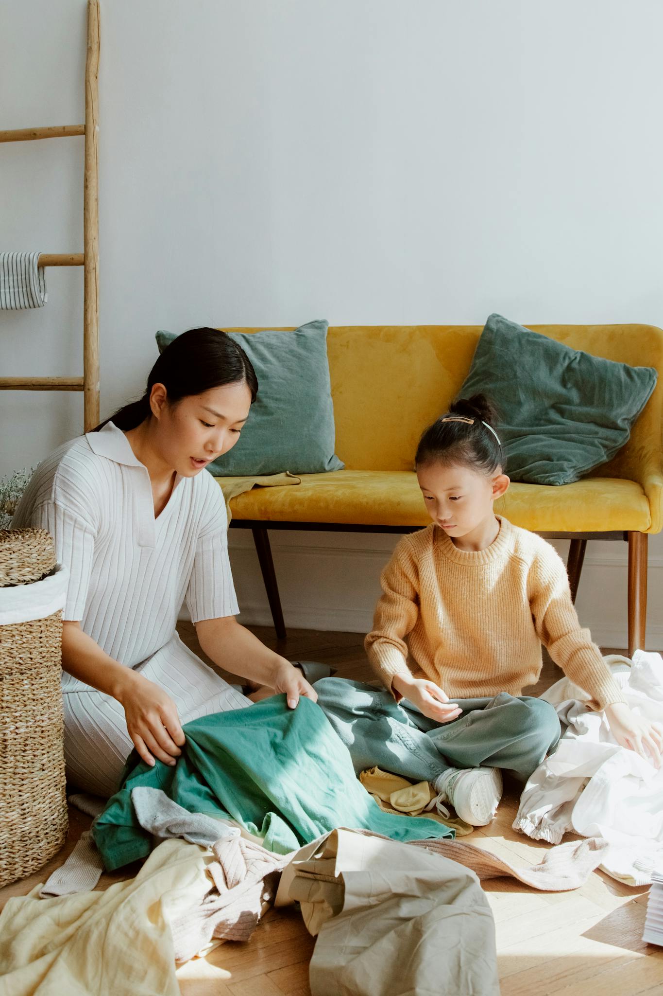 Asian mother and daughter sorting laundry together on the living room floor, showcasing family bonding and teamwork.